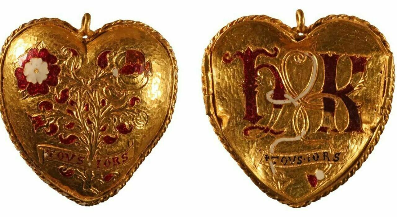 Medaglione d'oro a forma di cuore con disegni floreali e le iniziali "HR" in smalto rosso e bianco. Su entrambi i lati è presente un nastro con la scritta "TOVS IORS". Il medaglione ha bordi ornati e strutturati.