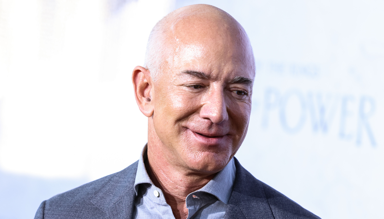 Jeff Bezos sorridente in abito grigio, fondatore di Amazon e analisi del suo patrimonio netto.