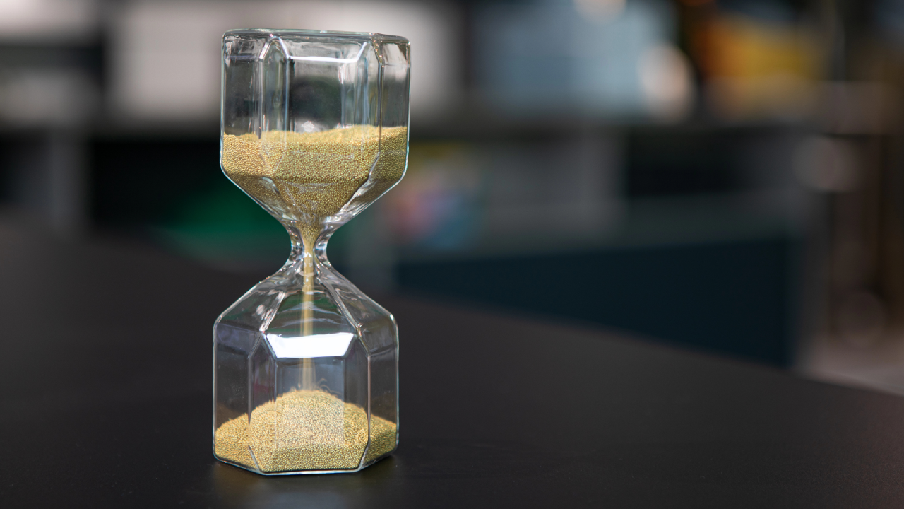 Clessidra moderna con frammenti d'oro che cadono su sfondo grigio neutro, metafora della liquidità nei private markets e del passaggio da Nav a Dpi.