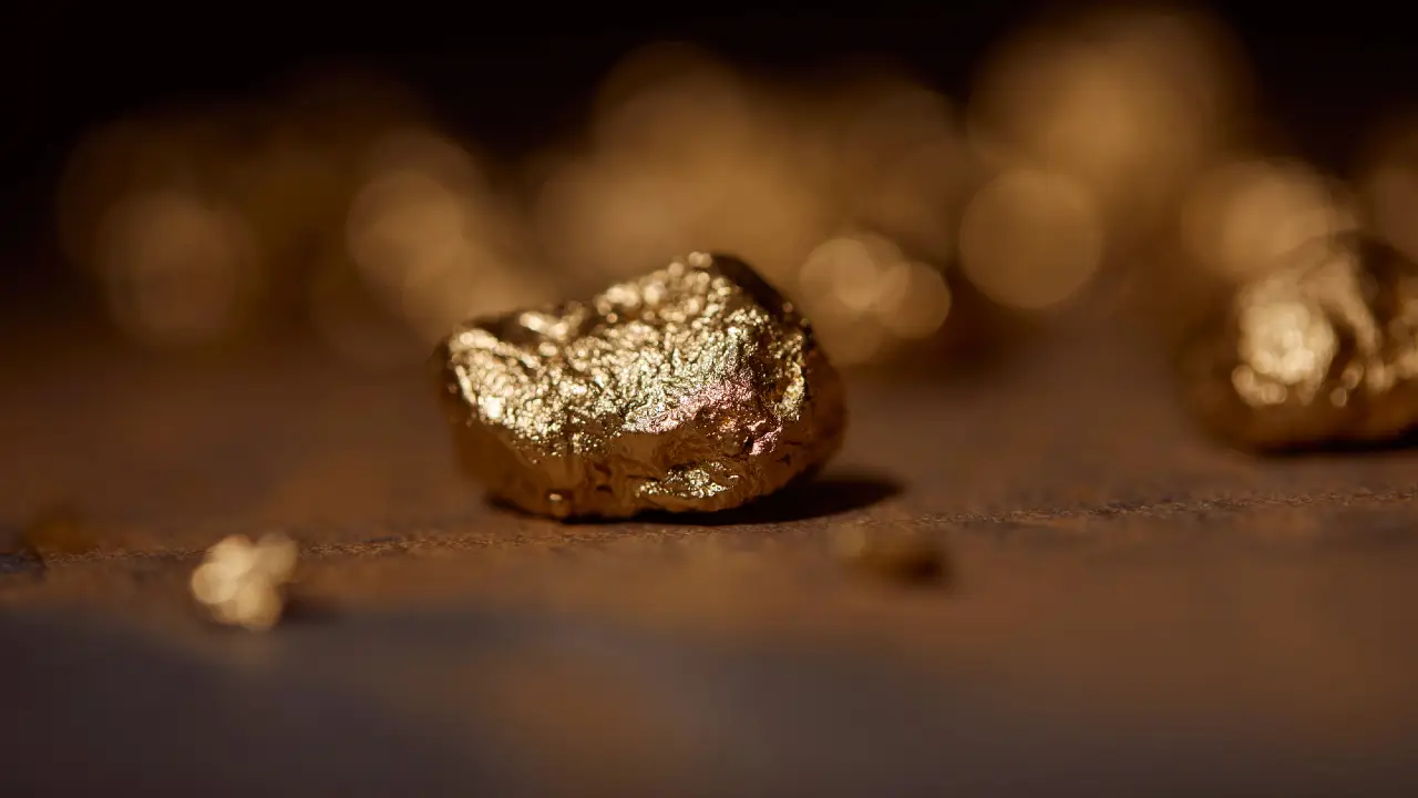 Foto ravvicinata di una pepita d'oro lucida appoggiata su una superficie liscia, con pepite d'oro sfocate sullo sfondo.