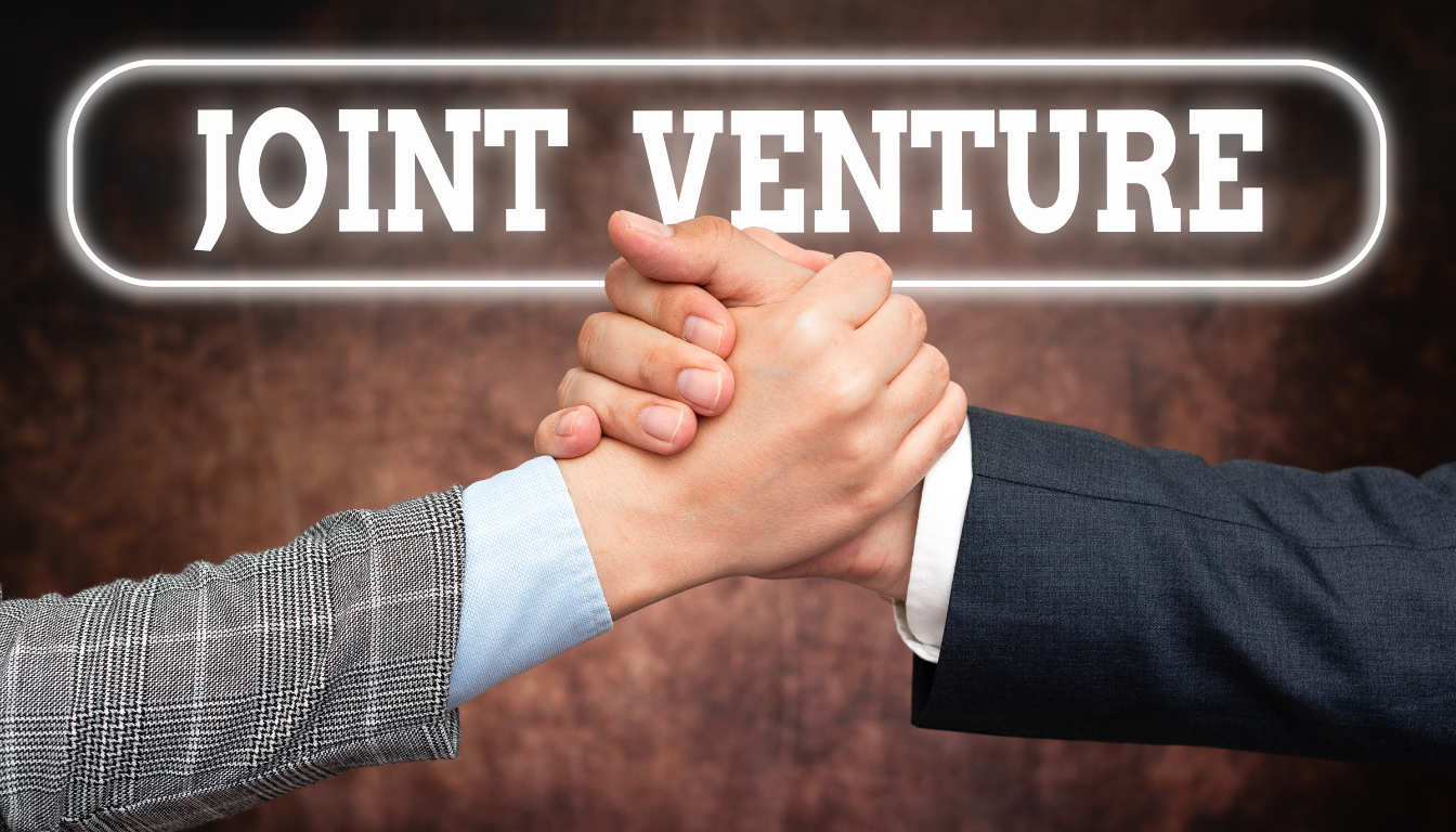 Due persone in abito da lavoro si stringono saldamente la mano, simbolo di partnership, con la scritta "JOINT VENTURE" che brilla sopra di loro su uno sfondo marrone strutturato.