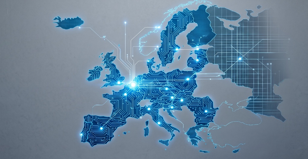 Mappa digitale dell'Europa composta da circuiti integrati e nodi luminosi blu su sfondo grigio istituzionale. Lo stile è minimalista, con un piano in cemento in primo piano che evoca solidità industriale e sovranità tecnologica.