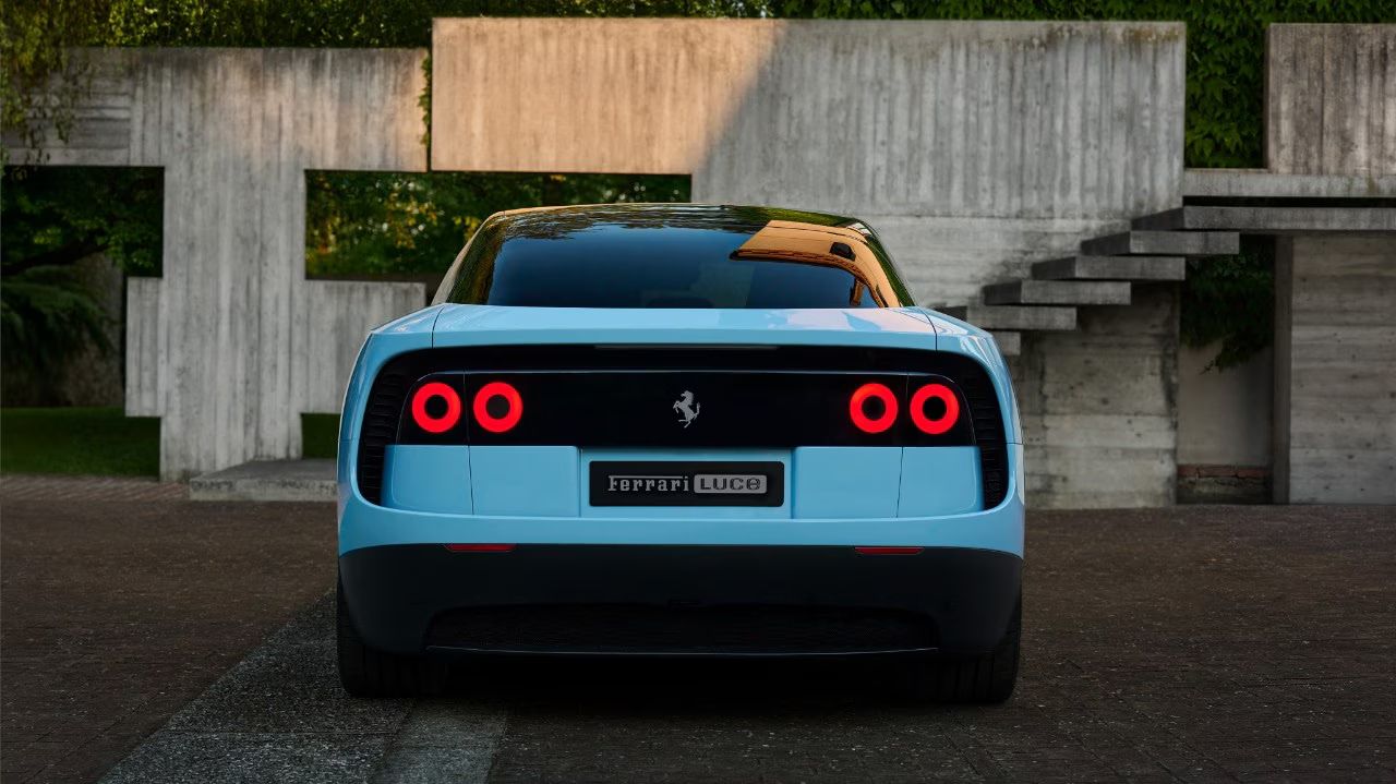Vista posteriore di un'auto azzurra "Ferrari Luce" con fanali accesi, sfondo di cemento e vegetazione.