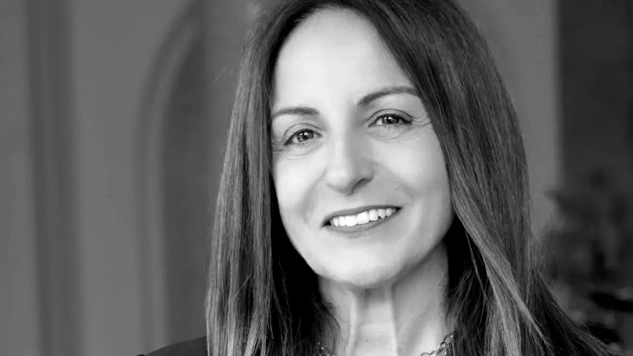 Ritratto in bianco e nero di una donna sorridente con lunghi capelli lisci e una collana.