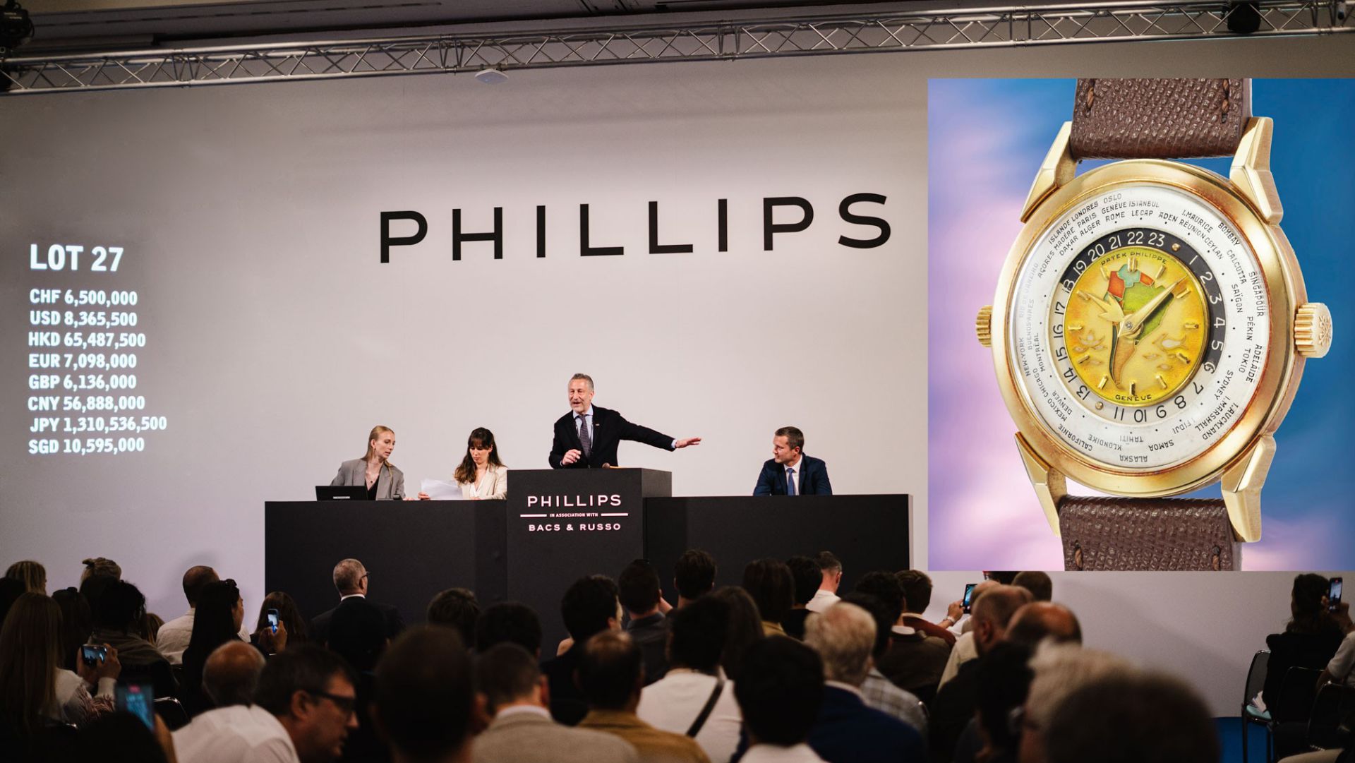 Asta Phillips con banditore, assistenti, pubblico e proiezione di prezzi e orologio di lusso.