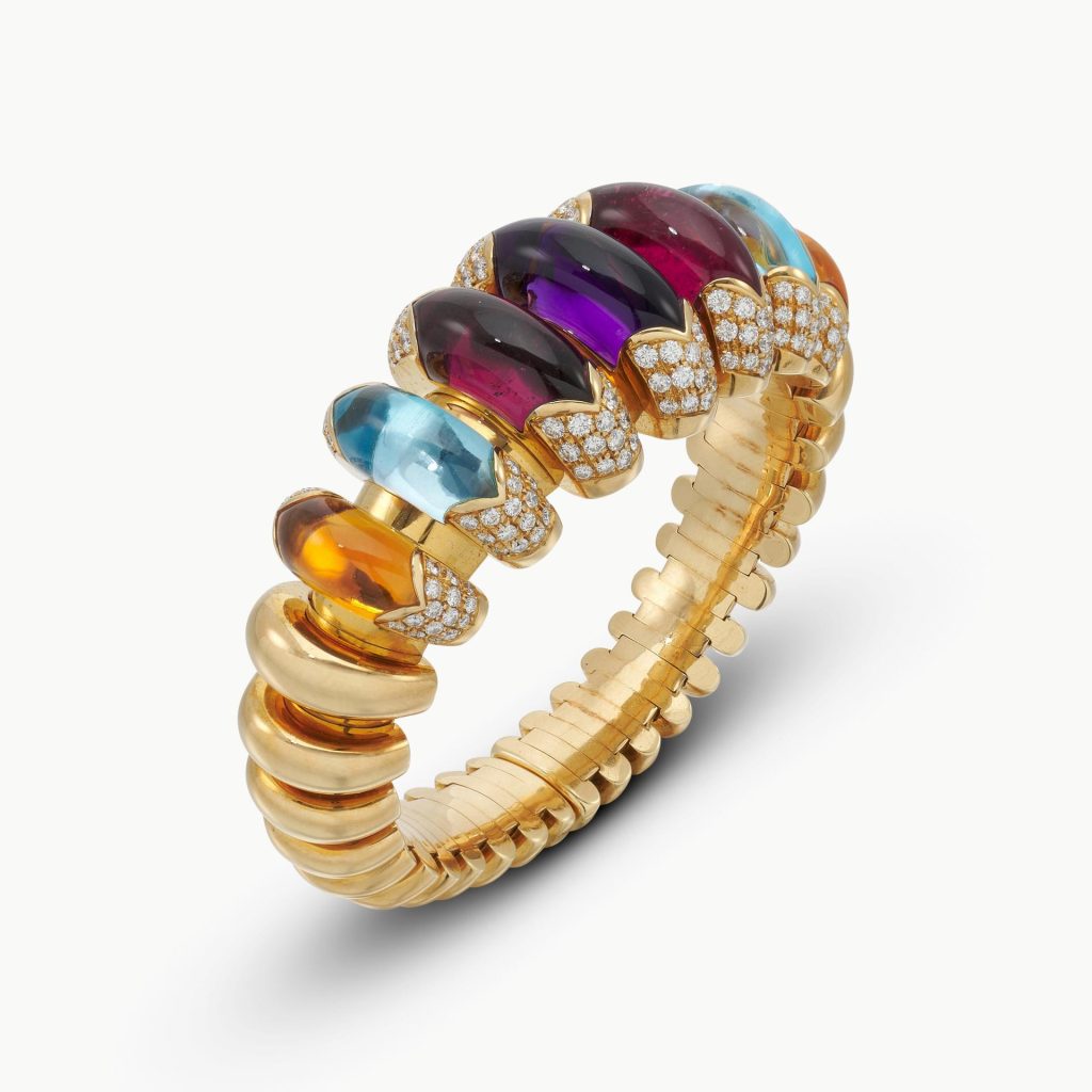 Bracciale d'oro con pietre preziose colorate e diamanti su sfondo bianco.