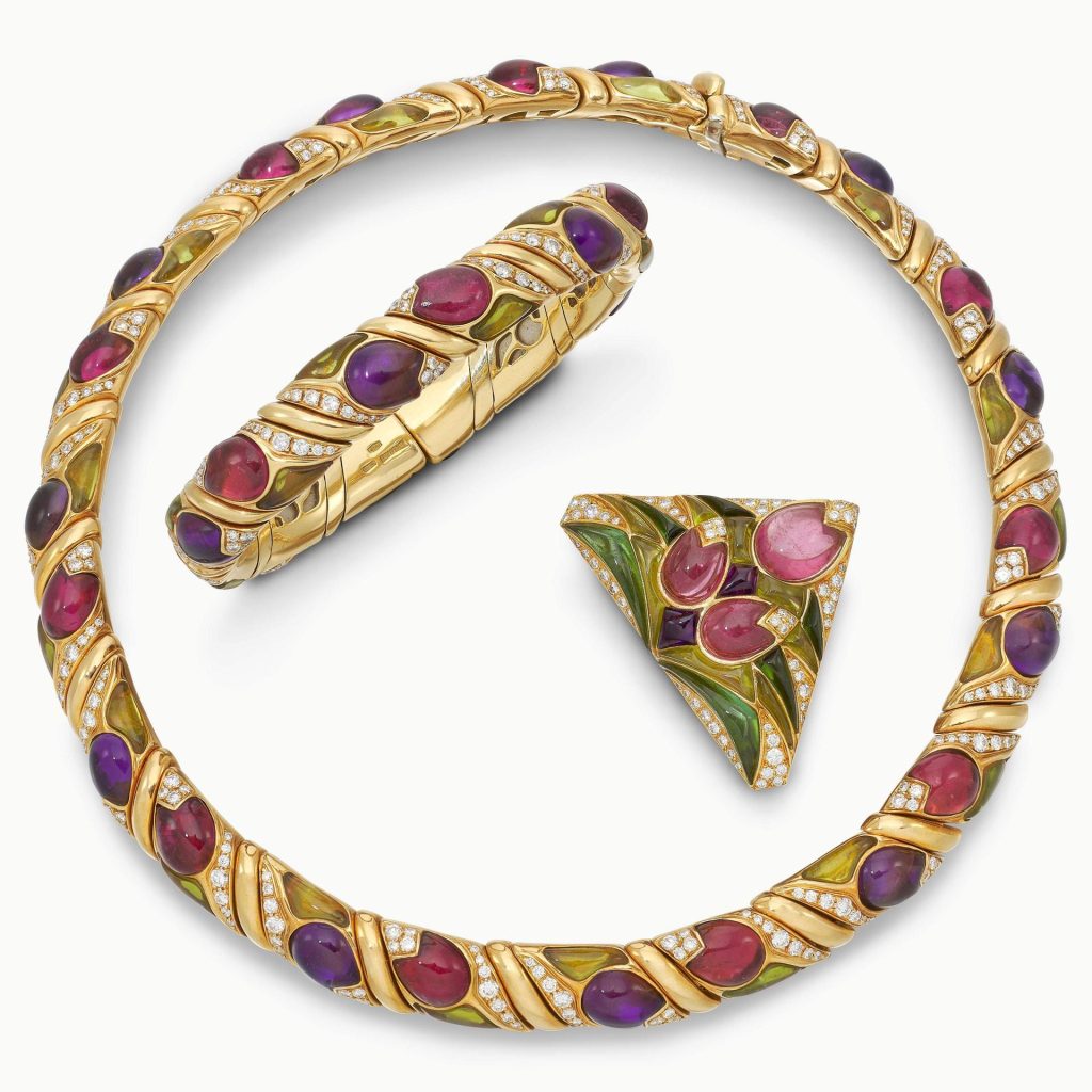Parure di gioielli in oro con gemme colorate e diamanti: collana, bracciale rigido e spilla triangolare.