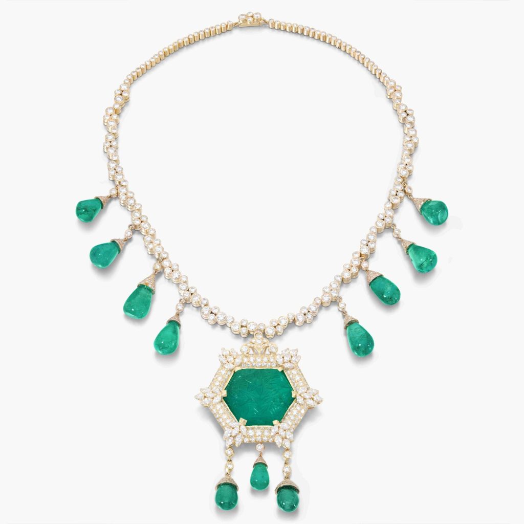 Collana d'oro con diamanti e smeraldi a goccia, con pendente esagonale smeraldo intagliato, su sfondo bianco.