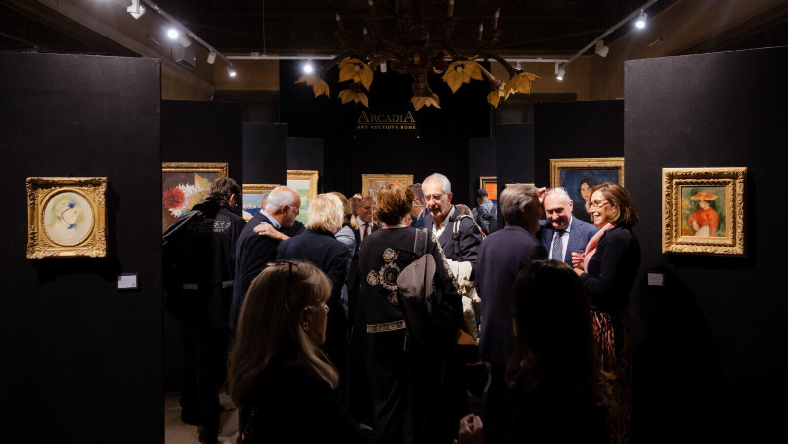 Persone in galleria d'arte, quadri incorniciati su pareti nere, lampadario dorato, insegna "Arcadia Art Auctions Rome".