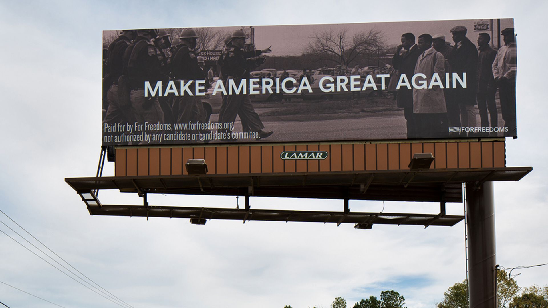 Un cartellone pubblicitario mostra una foto in bianco e nero di persone che affrontano poliziotti armati, con la scritta "Arte Difesa Diritti" e il testo in grassetto "Rendiamo l'America di nuovo grande". Di seguito sono riportate le dichiarazioni di esclusione di responsabilità e il logo di For Freedoms.