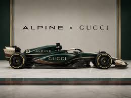 Auto da corsa verde e oro con scritte "Alpine x Gucci" su sfondo beige e verde.