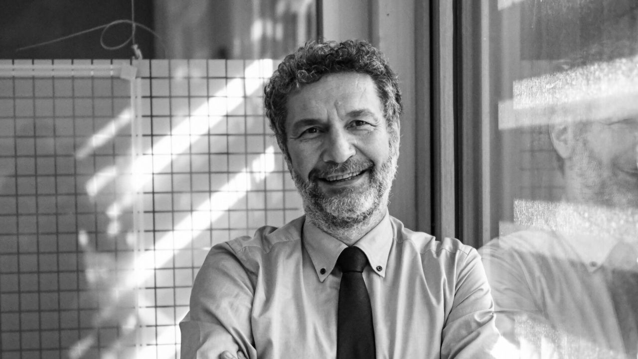 Ritratto in bianco e nero di uomo maturo sorridente con camicia e cravatta, riflesso su vetro.
