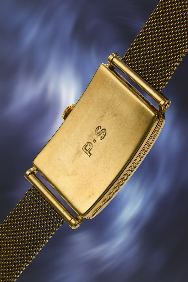 Retro di orologio dorato con cinturino a maglia, iniziali "P.S." incise e decorazione sul bordo.