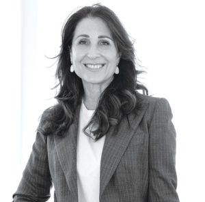 Ritratto in bianco e nero di una donna sorridente con blazer gessato e orecchini pendenti. Capelli lunghi e mossi.