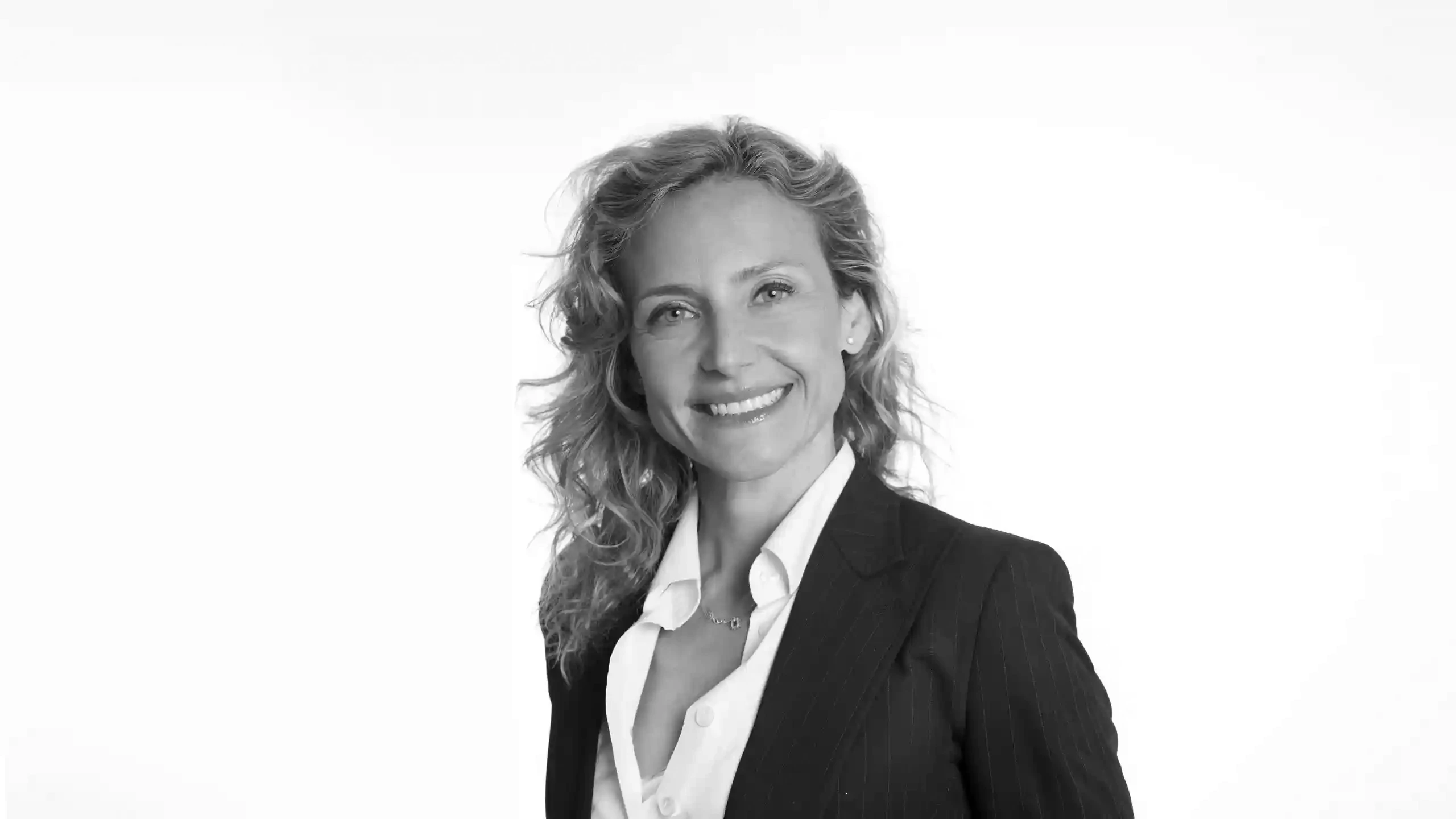 Ritratto in bianco e nero di una donna sorridente con capelli ricci, camicia bianca e giacca gessata.