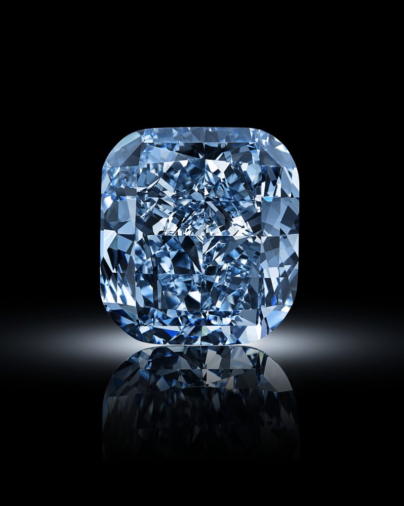 Diamante blu taglio cuscino su sfondo nero lucido, con riflesso speculare.