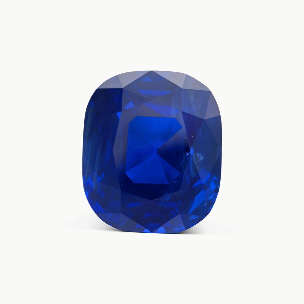 Gemma blu intenso, taglio cuscino, sfaccettata, su sfondo bianco. Riflessi luminosi e ombreggiature definiscono la forma.