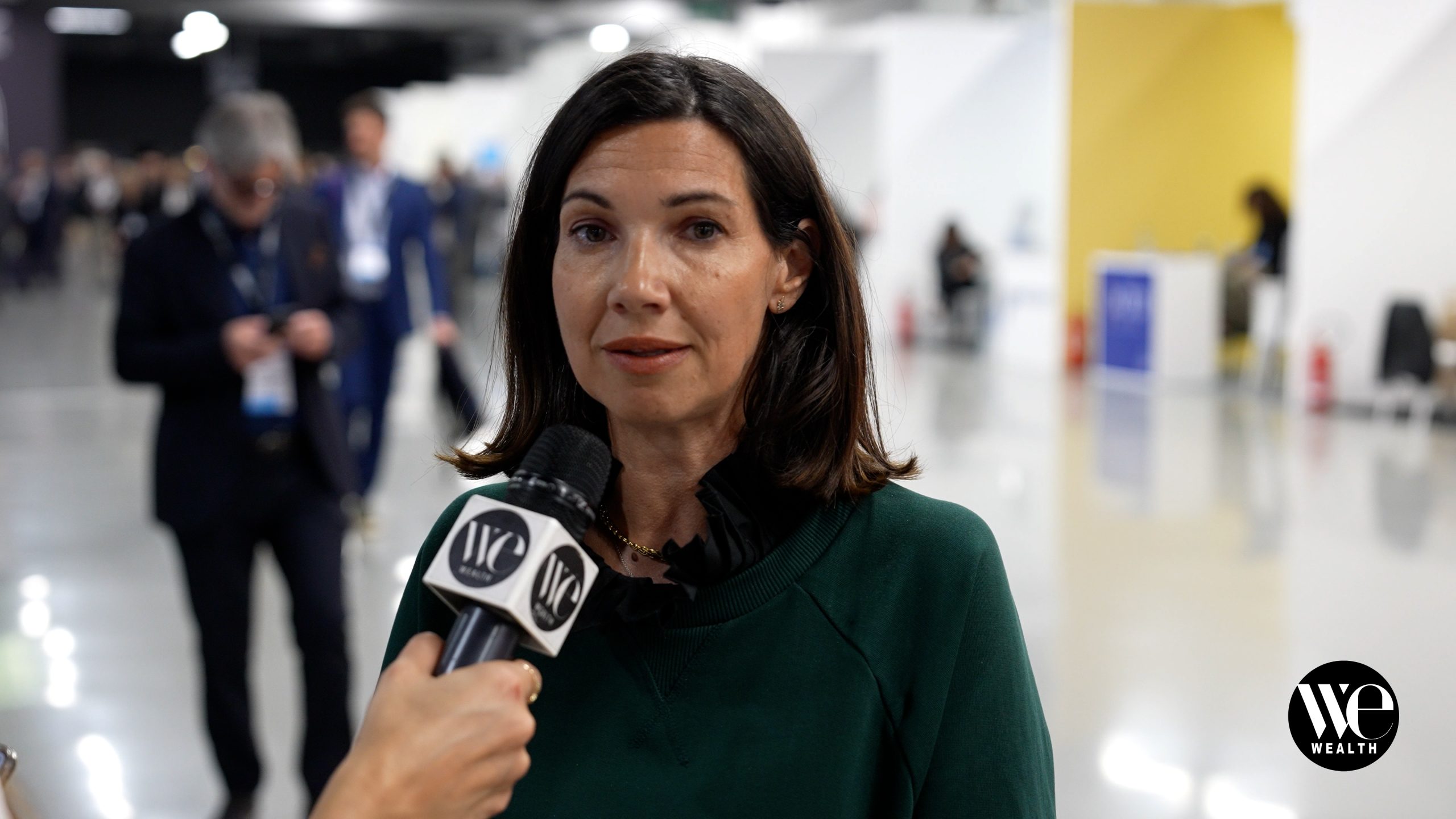 Roberta Zurlo di Banca Widiba intervistata con microfono "WE Wealth" in ambiente affollato e luminoso.