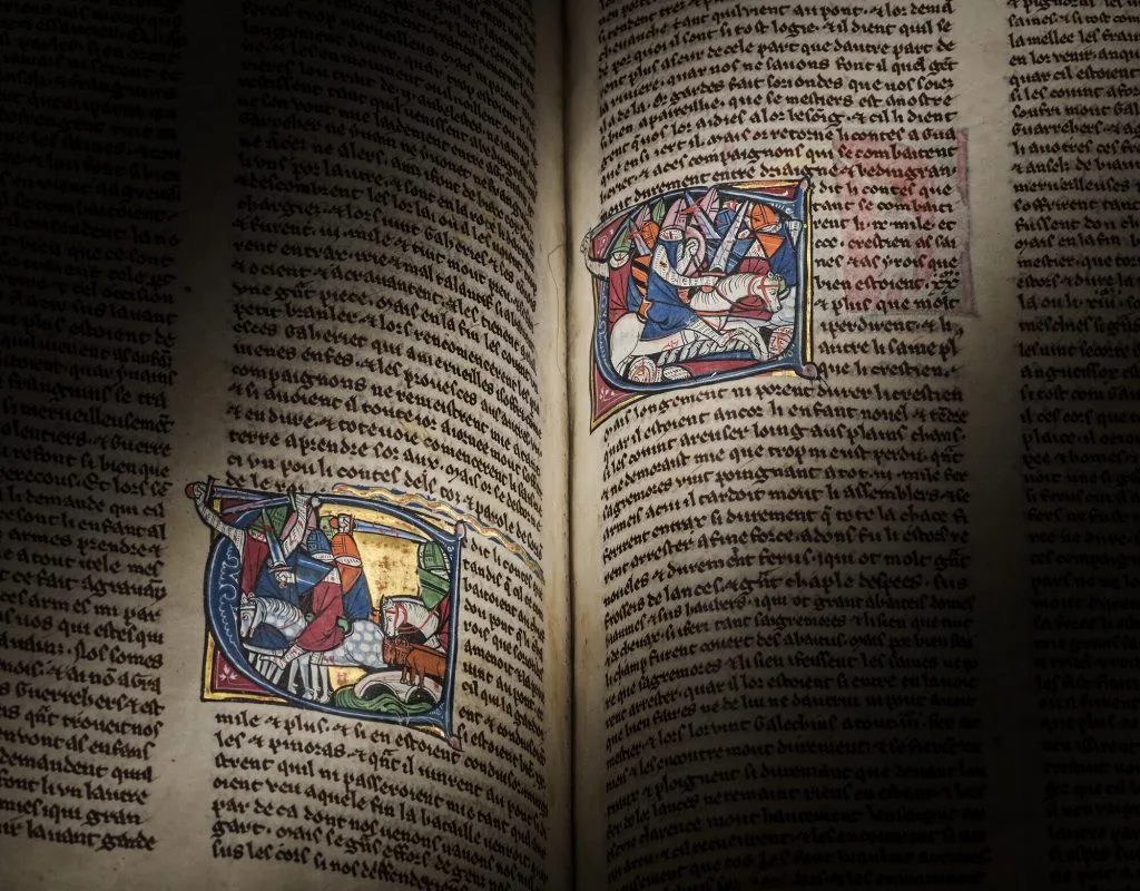 Pagine aperte di un libro antico con testo e illustrazioni colorate di scene medievali.