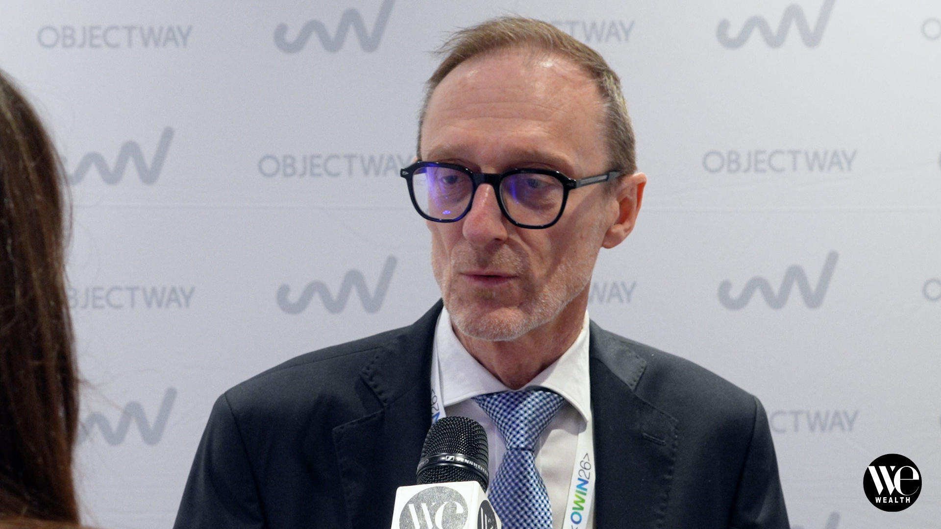 Uomo con occhiali e cravatta a quadri parla al microfono davanti a sfondo con logo "Objectway".
