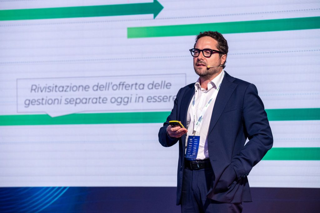 Uomo con occhiali parla davanti a schermo con testo "Rivisitzazione dell'offerta delle gestioni separate oggi in essere".