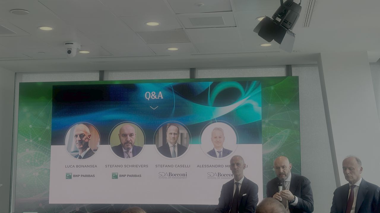 Schermo con "Q&A" e ritratti di relatori, con persone in primo piano.