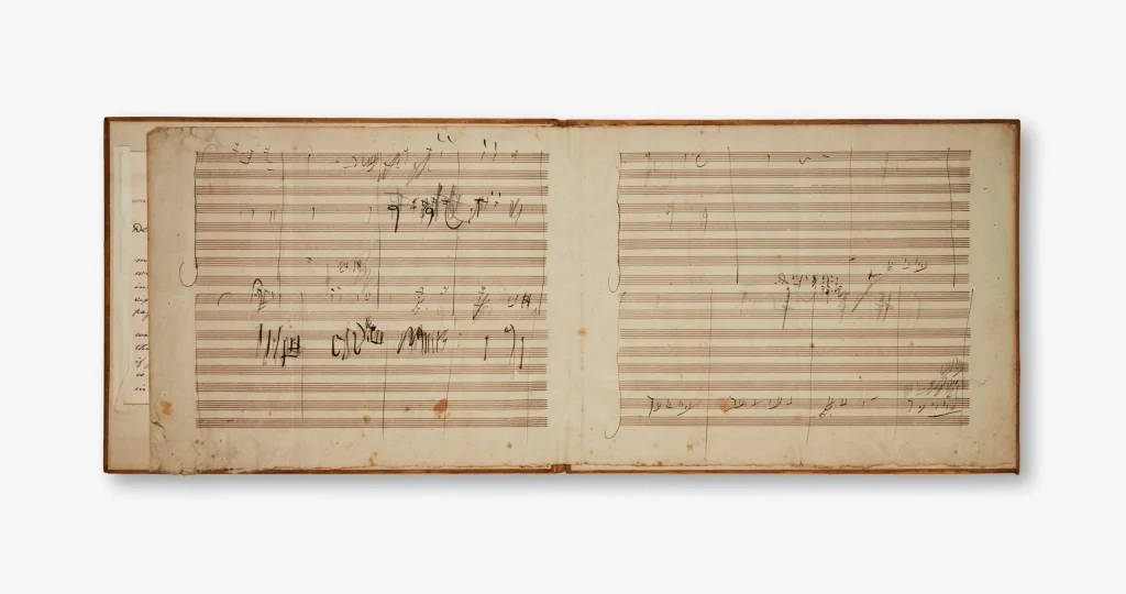 Un libro aperto mostra due pagine di spartiti musicali scritti a mano con inchiostro scuro su carta ingiallita.