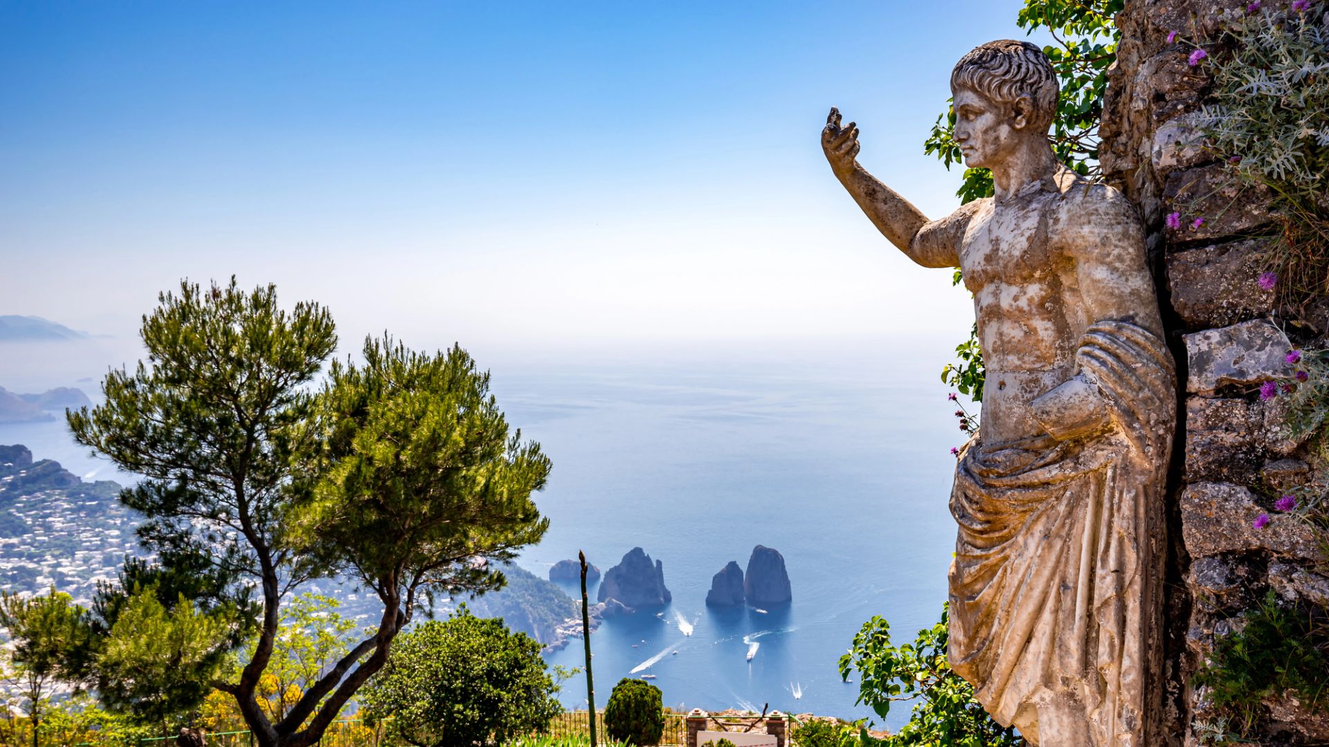 Statua antica su scogliera con vista sul mare e Faraglioni.