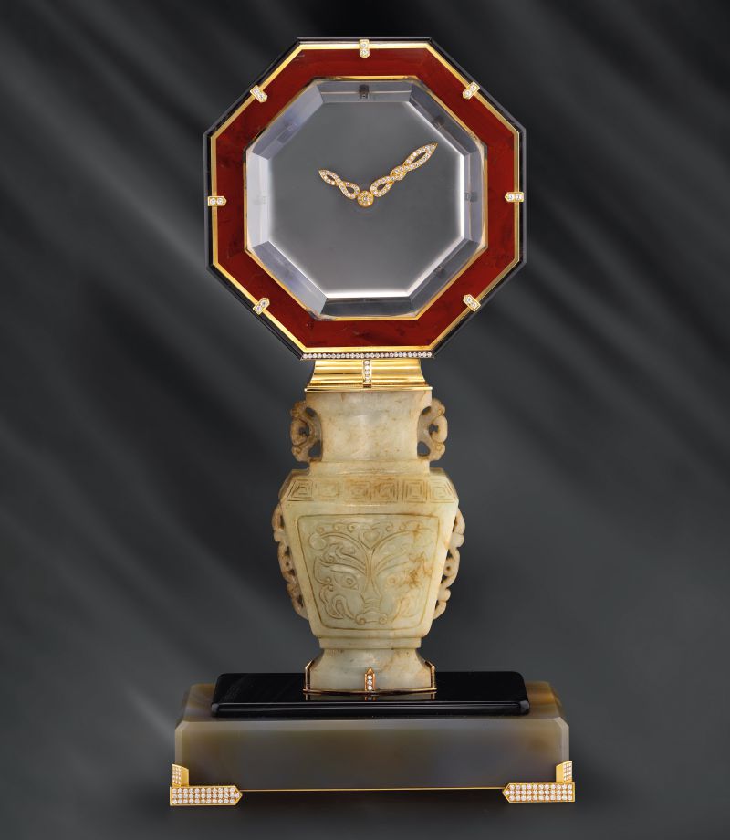 Orologio da tavolo ottagonale con cornice rossa, lancette ornate, base a vaso di giada e piedistallo decorato con diamanti.