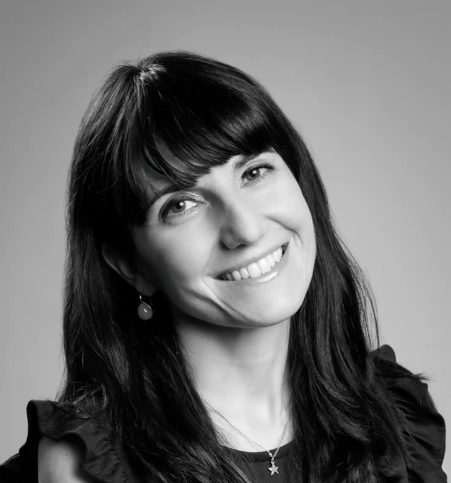 Donna sorridente con capelli scuri, orecchino a goccia e collana a stella.