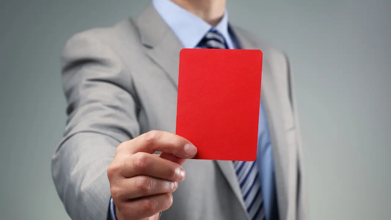 Uomo in giacca e cravatta mostra una carta rossa.