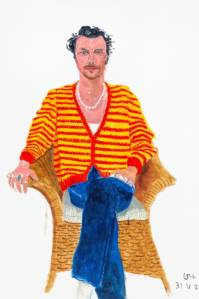 Ritratto di uomo con maglione a righe gialle e rosse, seduto su sedia di vimini.