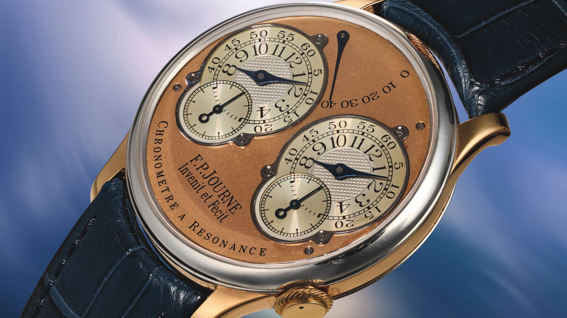 Orologio con quadrante color rame, due quadranti secondari, lancette blu e cinturino in pelle blu.