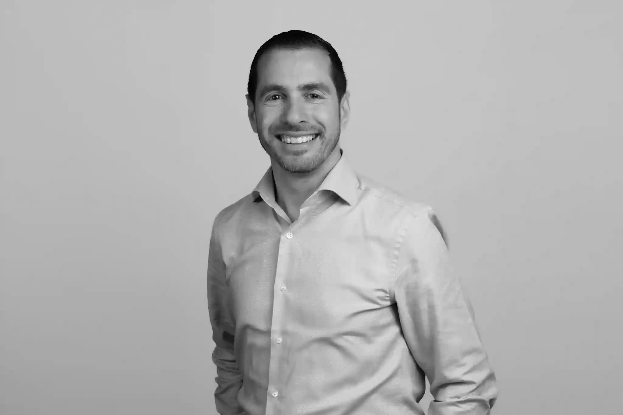Uomo sorridente con camicia chiara, in posa su sfondo grigio.