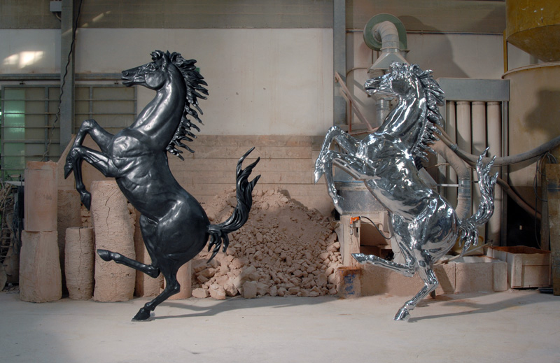 Due sculture di cavalli rampanti, una nera e una cromata, in un ambiente industriale.