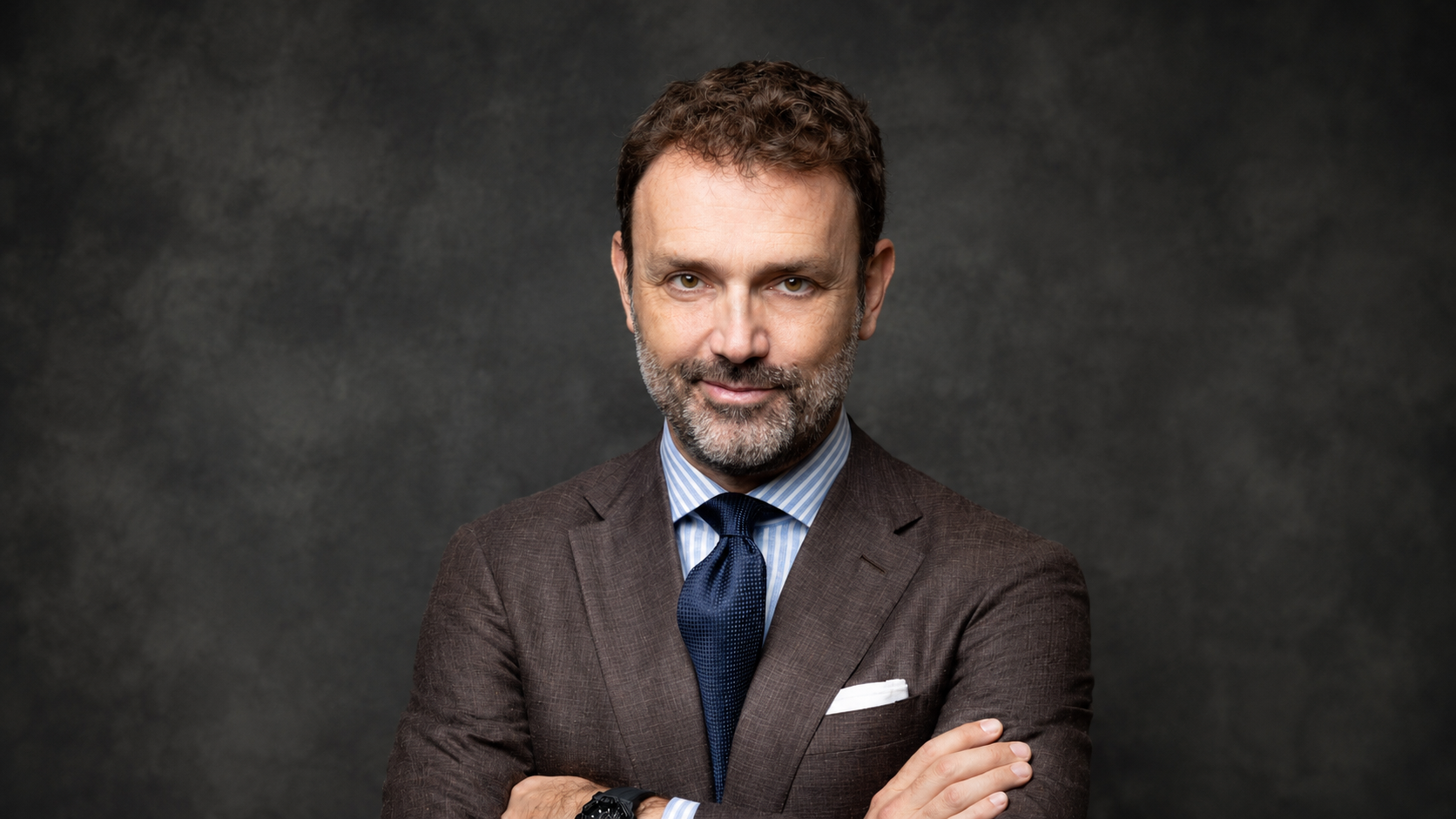 Uomo con abito marrone, camicia a righe azzurre e cravatta blu scuro.