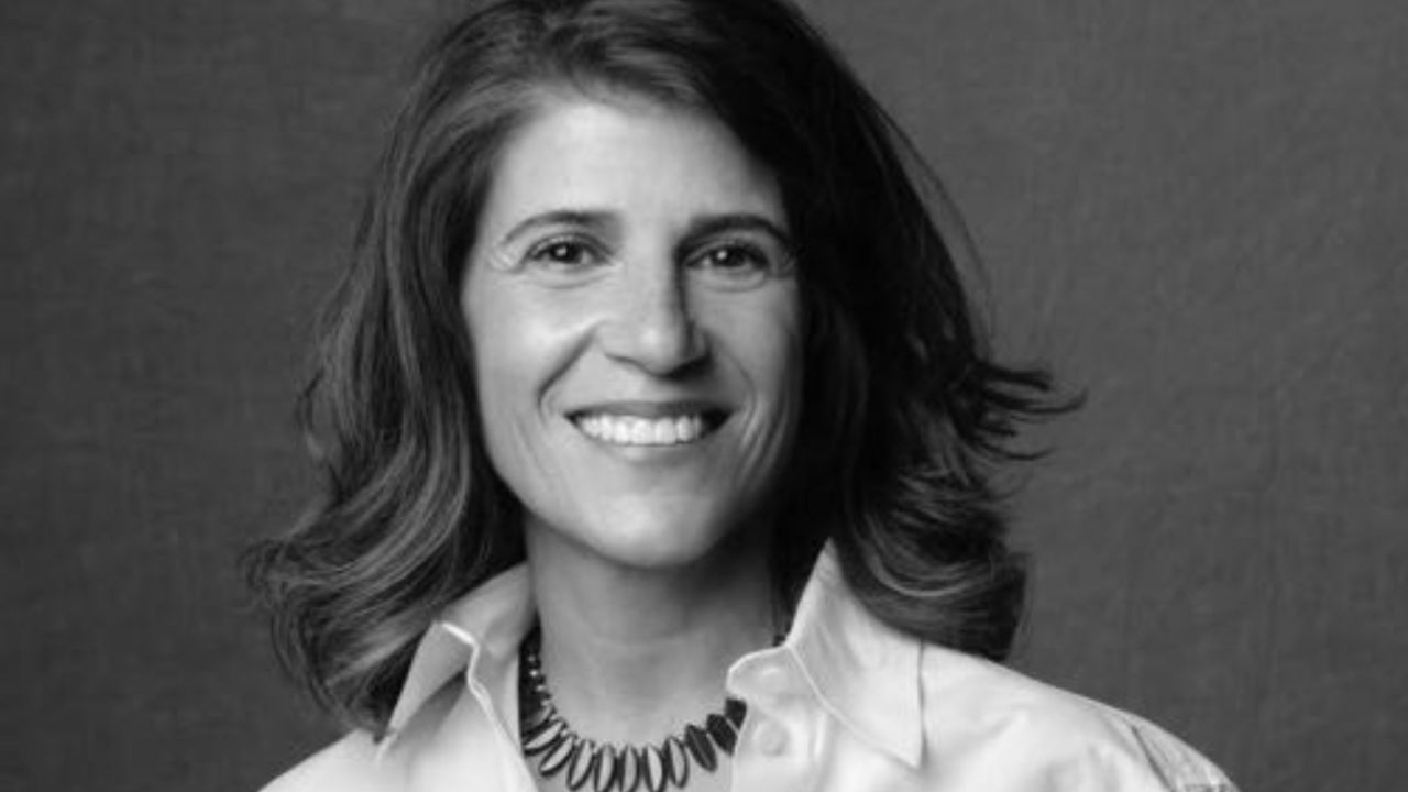 Donna sorridente con capelli mossi, indossa una camicia bianca e una collana.