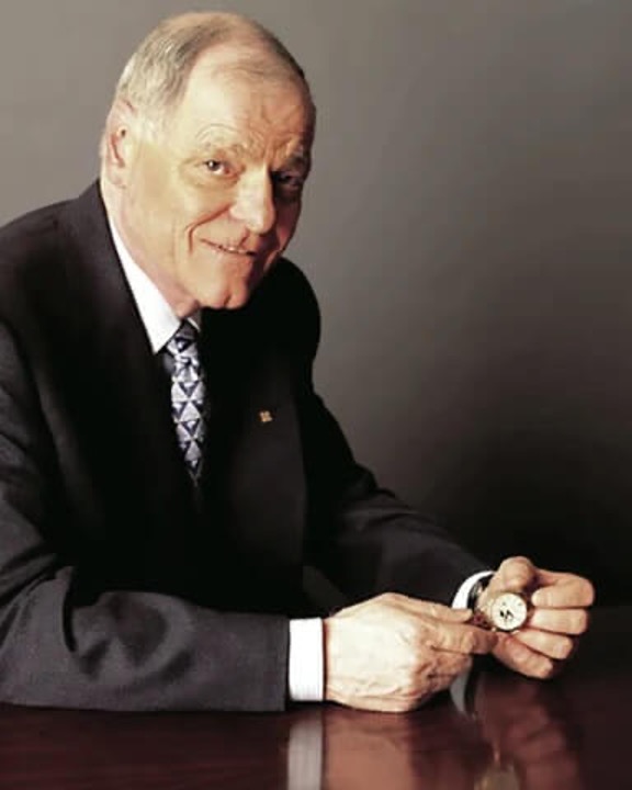 Uomo anziano in giacca e cravatta, tiene in mano un orologio da taschino.