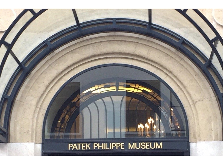 Ingresso ad arco del Patek Philippe Museum con insegna dorata e lampadari visibili all'interno.