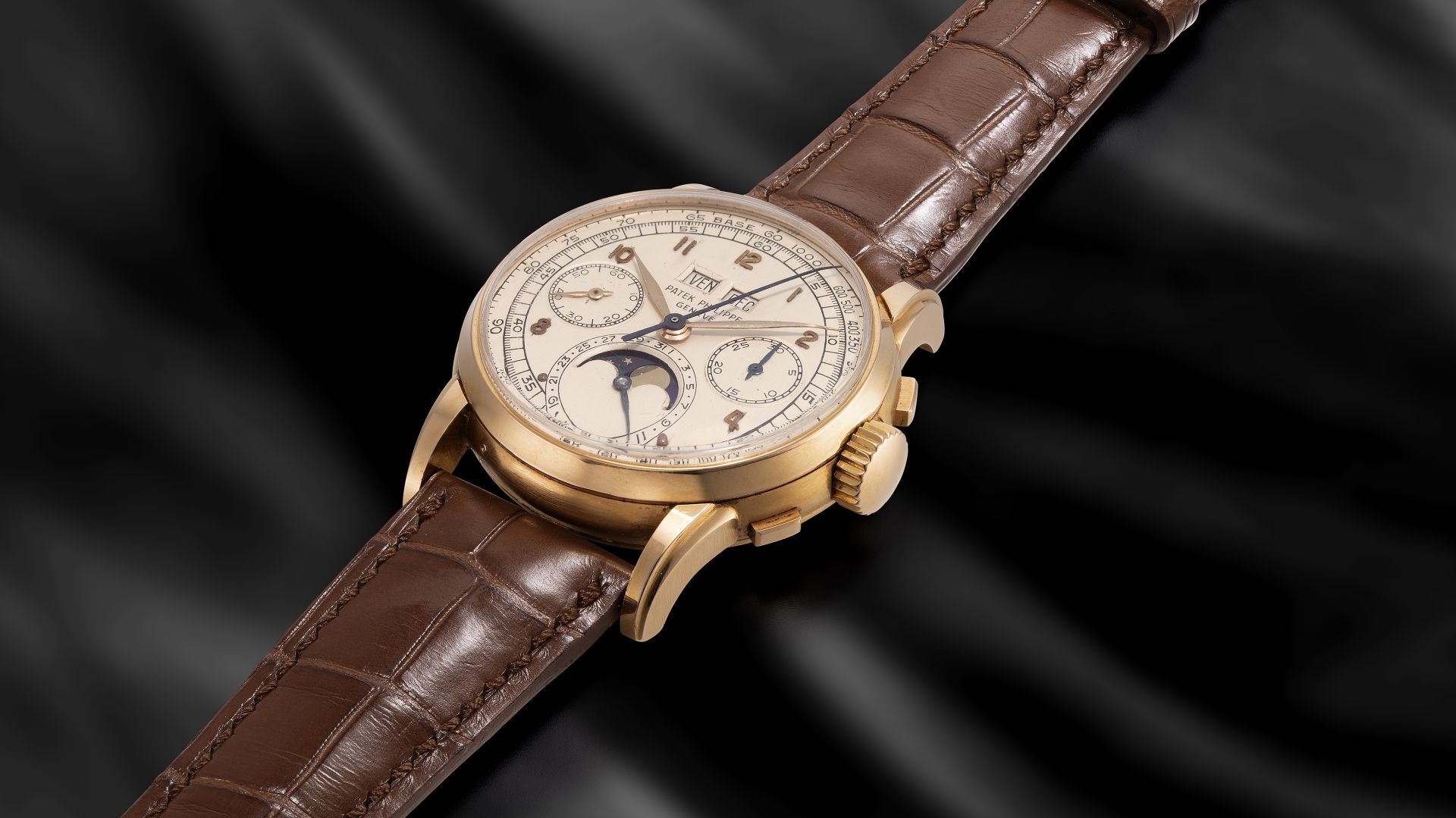 Orologio da polso dorato con cinturino in pelle marrone, quadrante avorio e indicatore fasi lunari su sfondo nero.