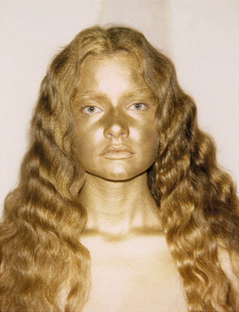 Volto e capelli di una persona con la pelle dipinta d'oro.