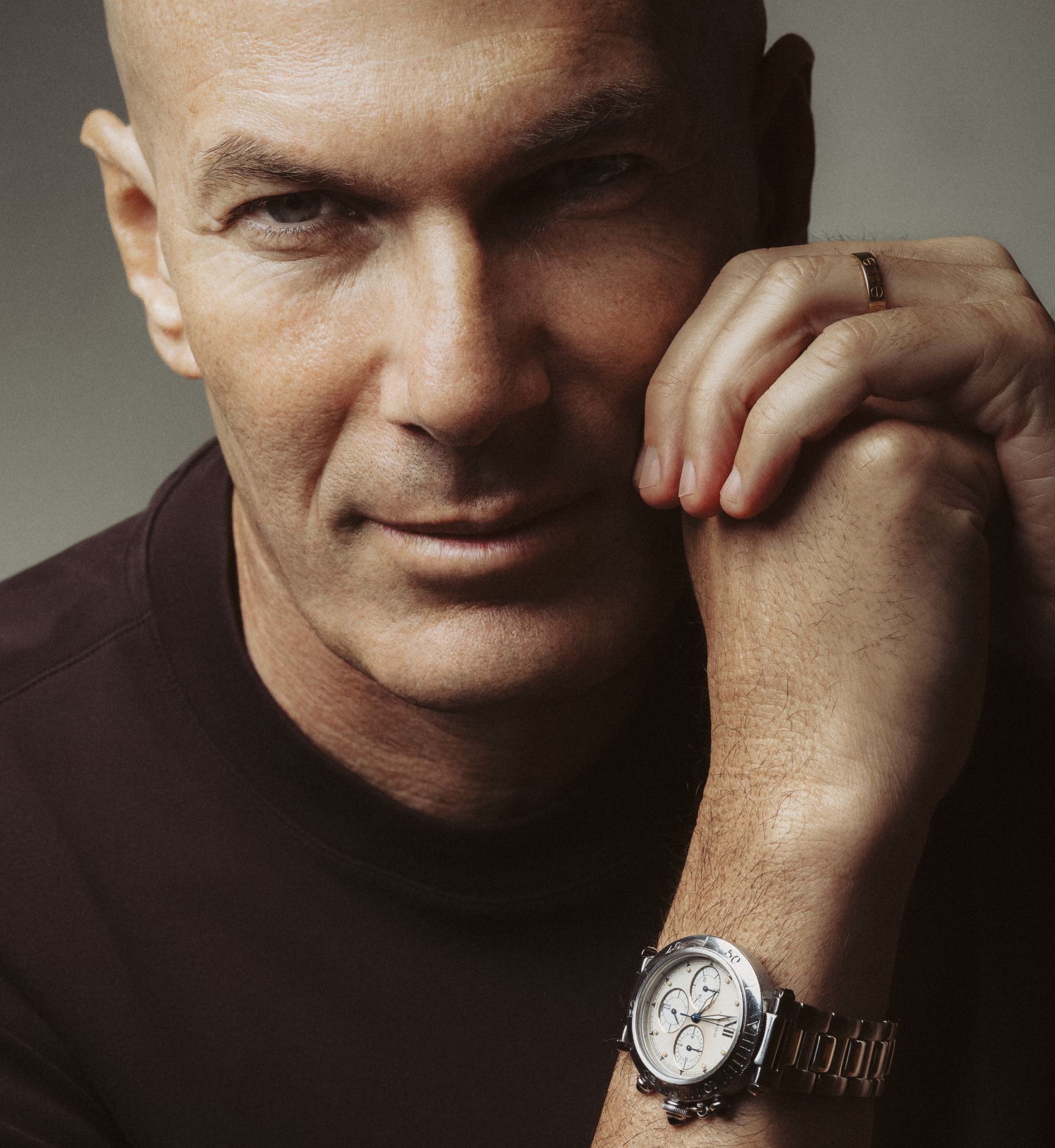 Uomo calvo con orologio da polso e anello d'oro, appoggia la mano sul viso.