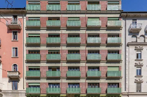 Facciata di un edificio con mattoni rossi, balconi verdi e finestre.