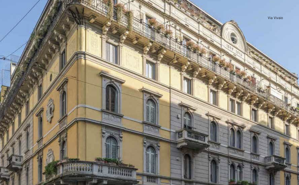Edificio storico giallo e grigio con balconi fioriti e finestre ad arco.