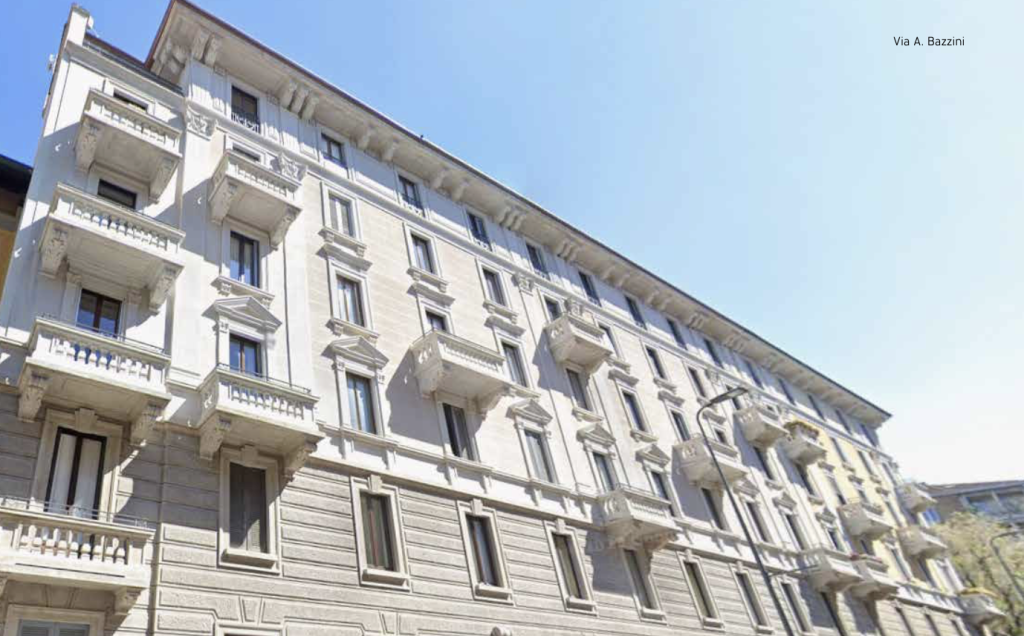Edificio bianco con balconi sporgenti e finestre, sotto un cielo azzurro.