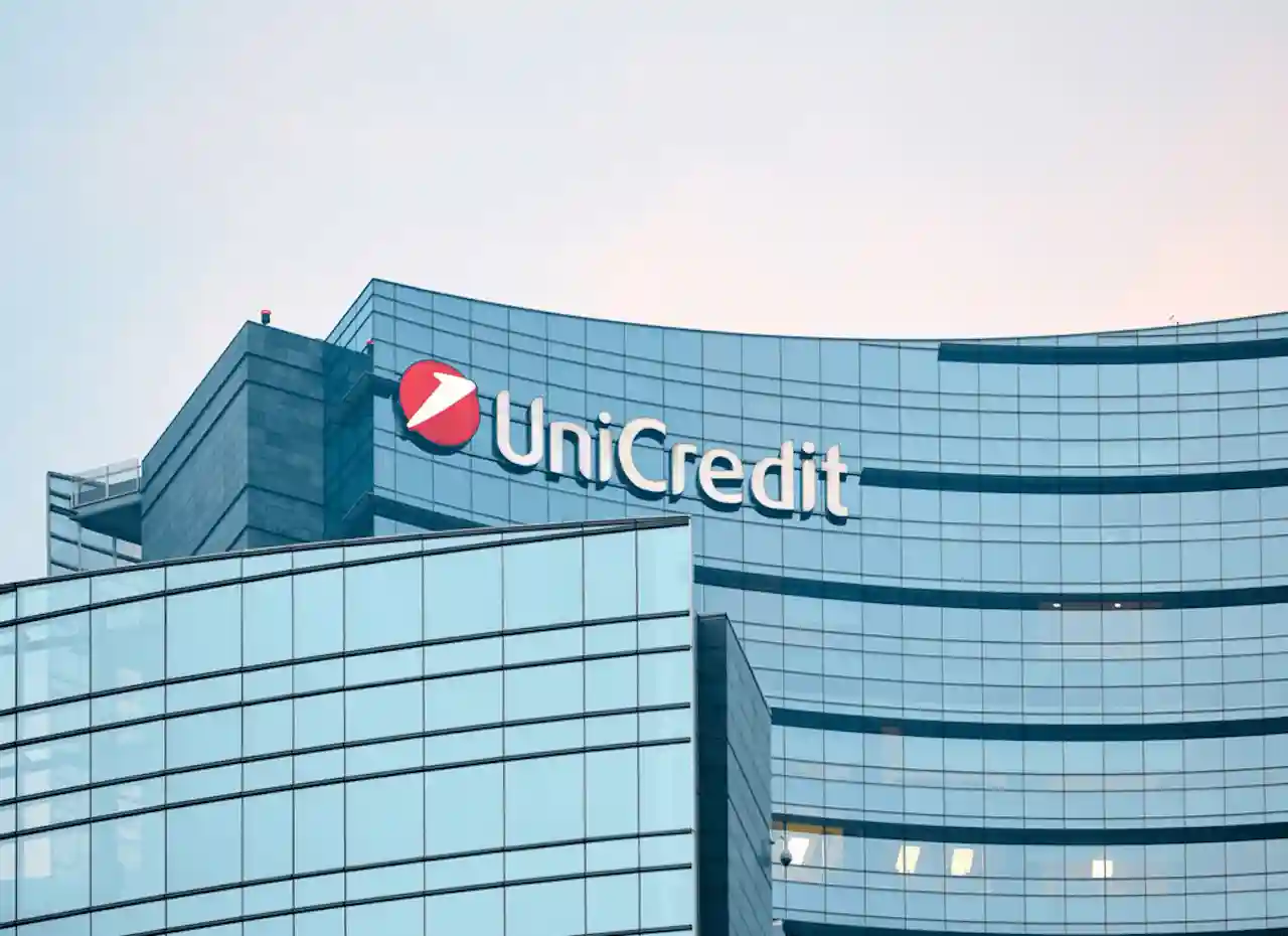 Edificio moderno con logo UniCredit illuminato. Vetrate blu riflettono il cielo.