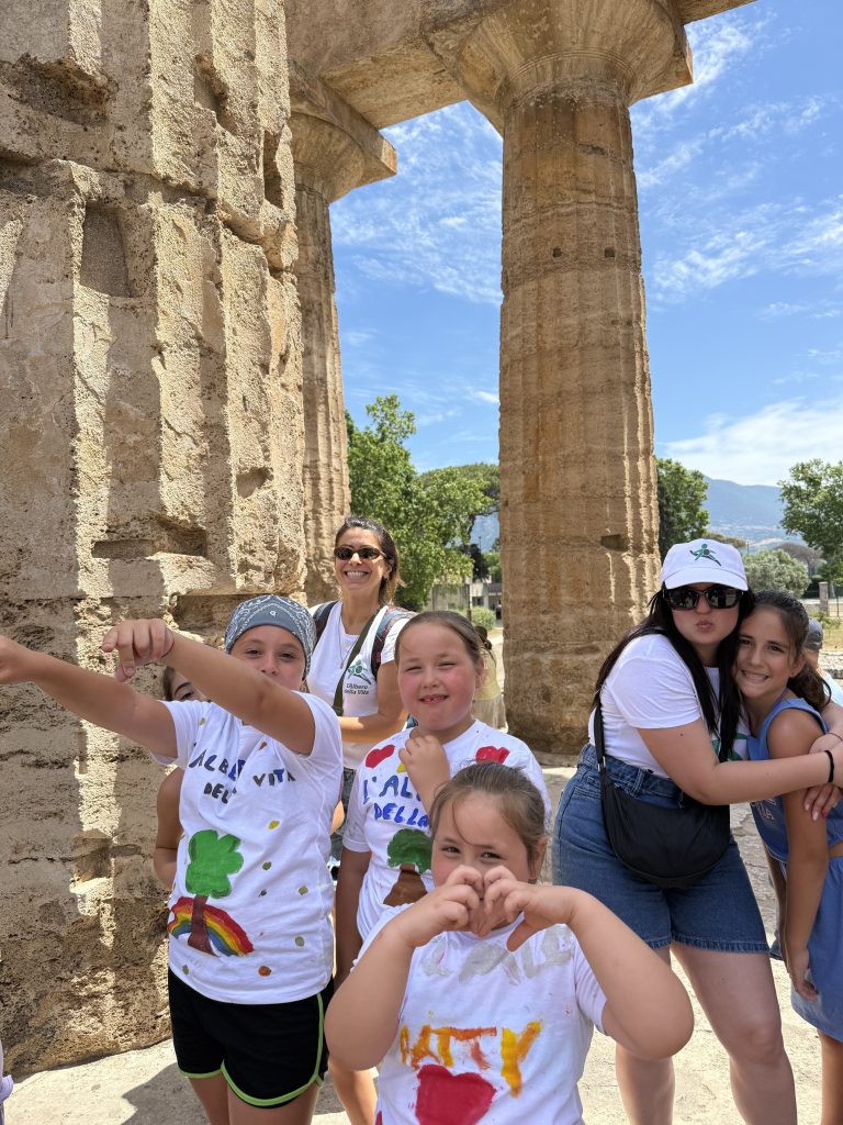Bambini sorridenti con magliette decorate, sotto antiche colonne greche.