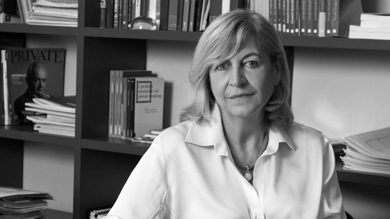 Donna con camicia bianca e collana, circondata da libri e riviste.