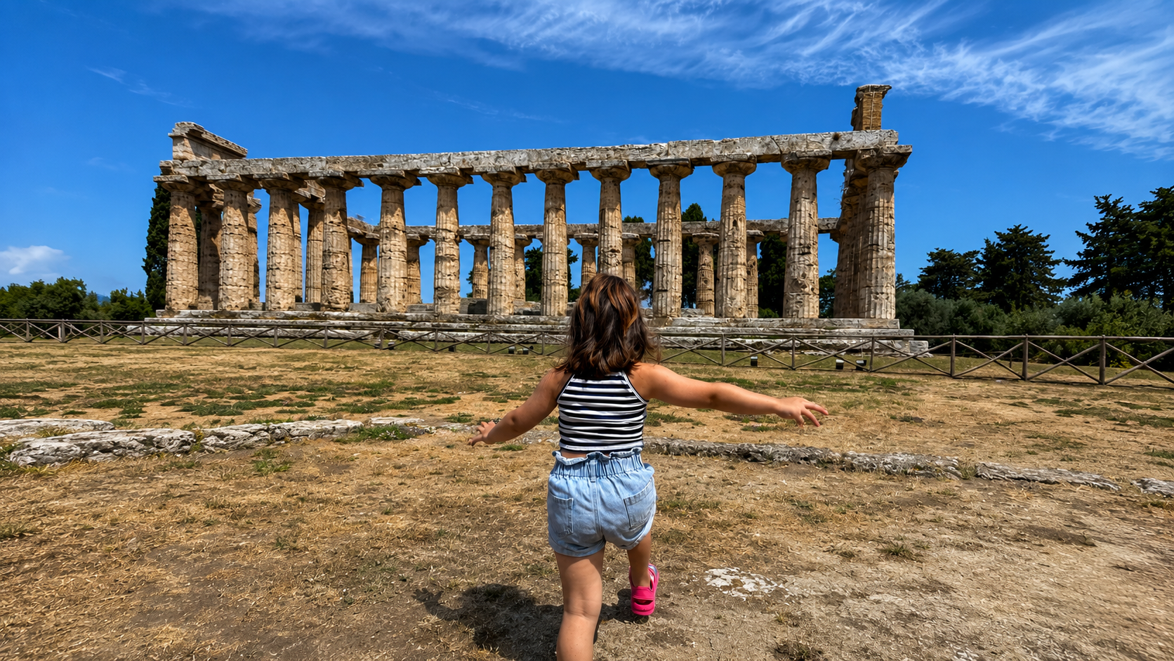 Bambina con braccia aperte davanti a un tempio greco con colonne.