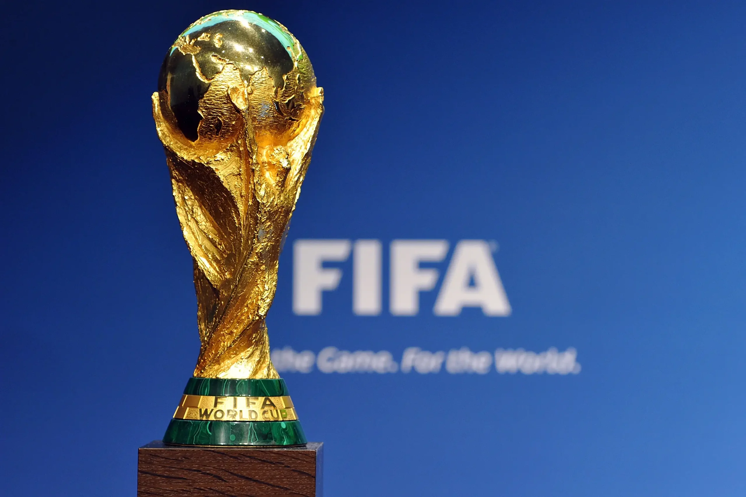 Trofeo FIFA World Cup dorato su sfondo blu con logo FIFA sfocato.